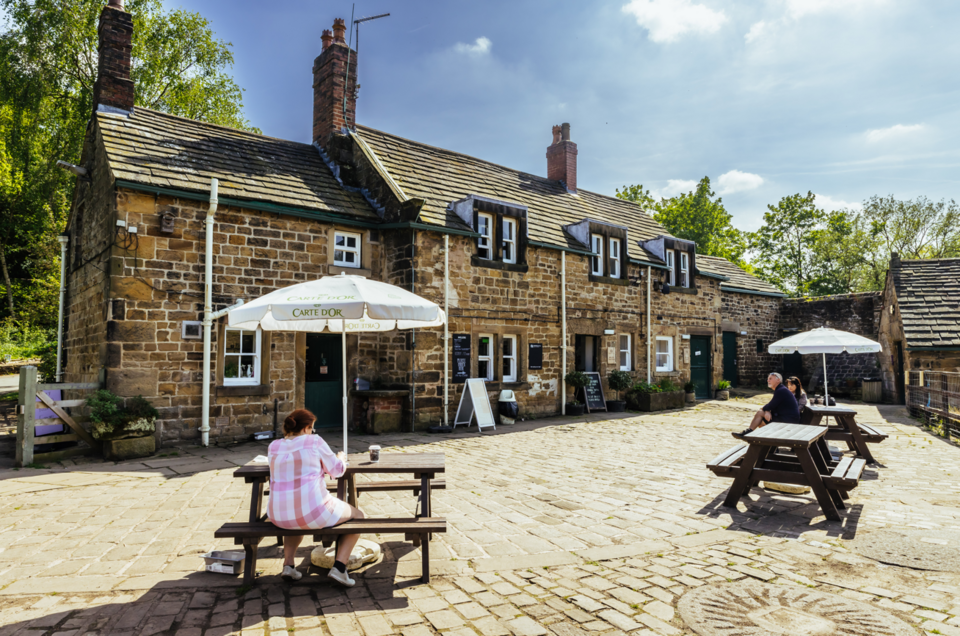 Three visitors sat down on benches drinking cups of coffee at Worsbrough Mill